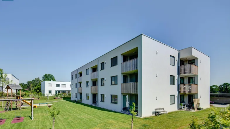 Modernes Mehrfamilienhaus mit Balkonen, umgeben von einer grünen Rasenfläche und einem Spielplatz.