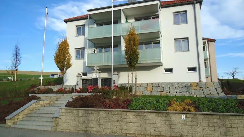 Modernes Mehrfamilienhaus mit Balkonen und gepflegter Außenanlage unter blauem Himmel.