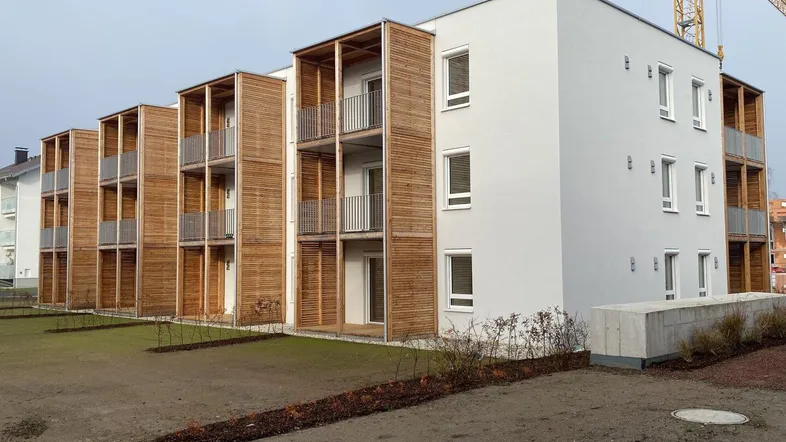 Neubau-Wohngebäude mit moderner Architektur, weißer Fassade und Holzverkleidung an den Balkonen.