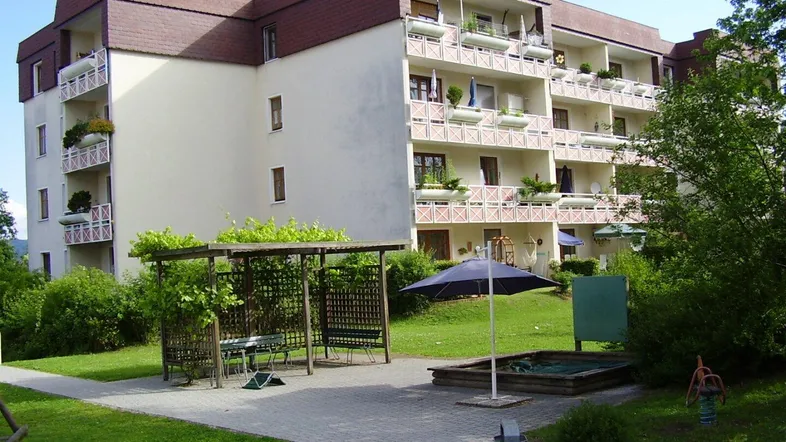 Mehrfamilienhaus mit mehreren Balkonen, umgeben von Grünflächen und einem Spielplatz für Kinder.