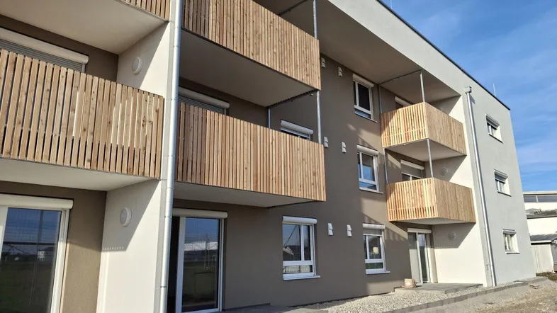 Moderne Wohnanlage mit mehreren Balkonen und Holzverkleidung unter blauem Himmel.