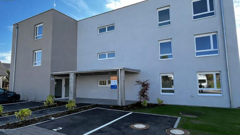 Modernes Mehrfamilienhaus mit heller Fassade, großen Fenstern und Parkplätzen im Freien.