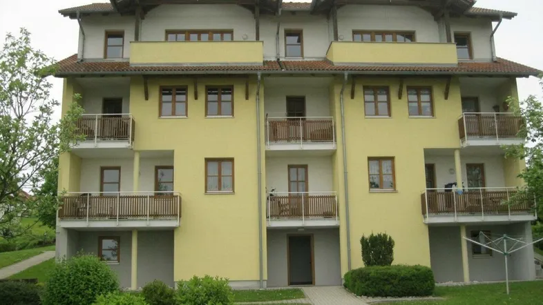 Mehrfamilienhaus mit gelber Fassade, mehreren Balkonen und gepflegter Grünanlage im Vordergrund.