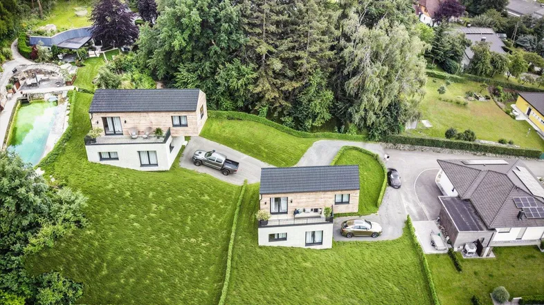 Luftaufnahme von zwei modernen Häusern mit großen Gärten und Zufahrten in grüner Umgebung.