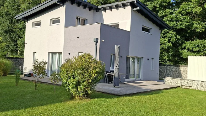 Modernes Einfamilienhaus mit heller Fassade, Holzterrasse und gepflegtem Gartenbereich.