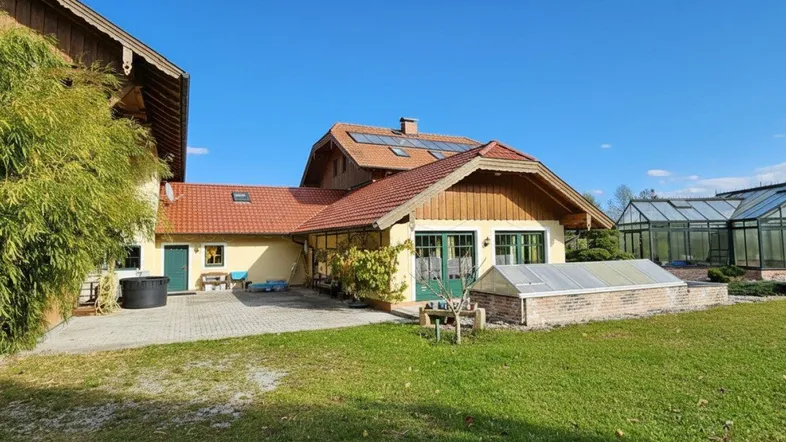 Großzügiger Gartenbereich mit Haupthaus, Gewächshaus und gepflegter Rasenfläche unter blauem Himmel.