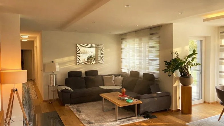 Helles Wohnzimmer mit großem Ecksofa, Holzboden und modernem Spiegel, durchflutet von Abendsonne.