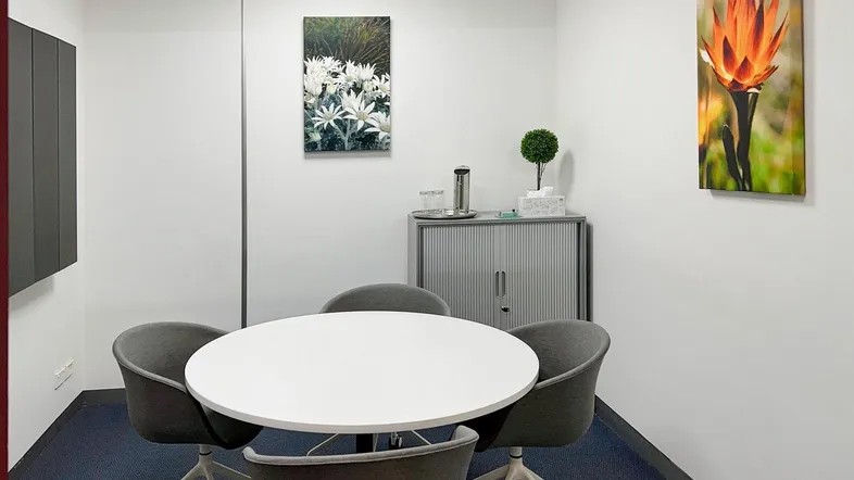 Kleiner Besprechungsraum mit rundem Tisch, vier Stühlen und minimalistischer Einrichtung für effiziente Meetings.