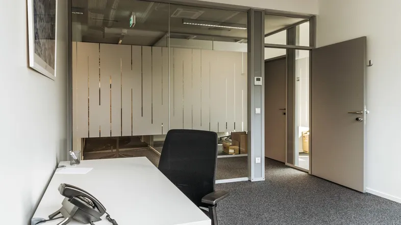 Modernes Büro mit Teppichboden und Glaswand, die einen weiteren Arbeitsbereich abtrennt.