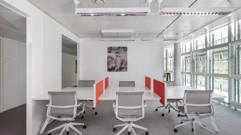 Moderner Großraumbüro-Arbeitsplatz mit mehreren Schreibtischen, ergonomischen Stühlen und großen Fenstern.