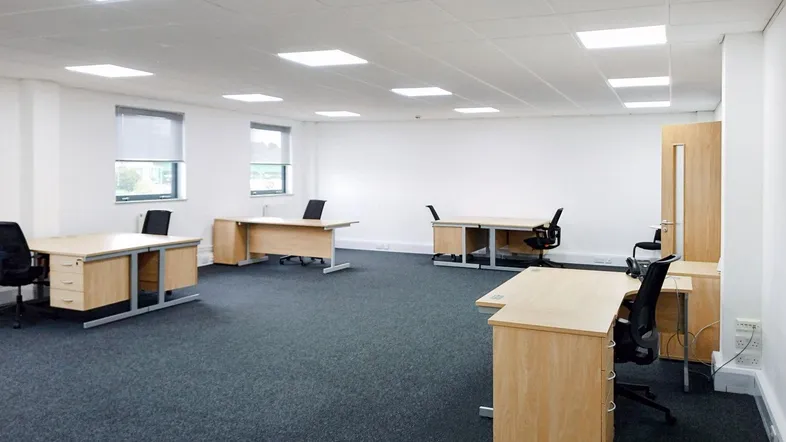 Geräumiges und helles Büro mit mehreren Schreibtischen, Teppichboden und großen Fenstern für natürliches Licht.