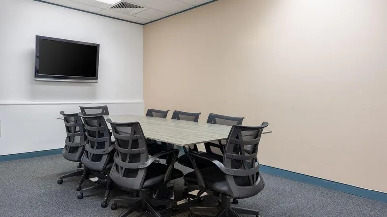 Moderner Konferenzraum mit großem Tisch, ergonomischen Stühlen und Wandfernseher für Präsentationen.