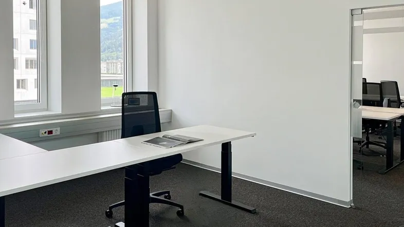 Modernes Büro mit höhenverstellbarem Schreibtisch, ergonomischem Stuhl und Blick auf die Berge.