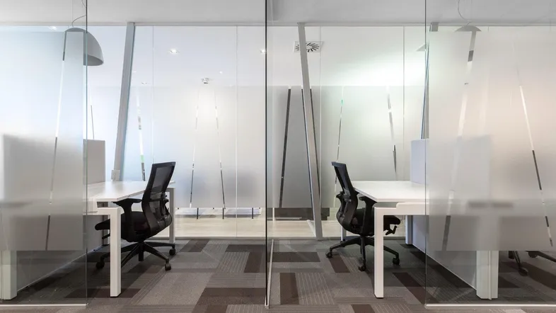 Moderner Büroraum mit Glaswänden, ergonomischen Stühlen und Teppichboden in neutralen Farben.