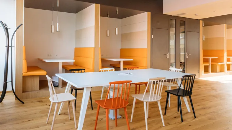 Modernes Büro mit verschiedenen Sitzbereichen, Holzboden und orangefarbenen Akzenten für flexible Arbeitsweisen.