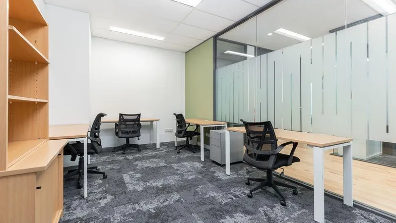 Modernes Großraumbüro mit mehreren Arbeitsplätzen, Teppichboden und Glaswänden für eine offene Atmosphäre.