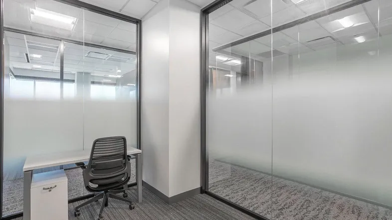 Modernes Büro mit Glaswänden und Teppichboden, ausgestattet mit einem Schreibtisch und Bürostuhl.