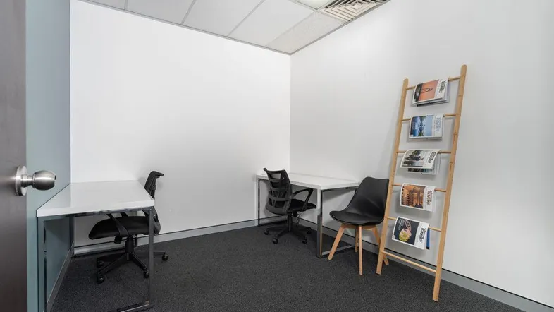 Kleines, helles Büro mit zwei Arbeitsplätzen, Teppichboden und einer Zeitschriftenablage.