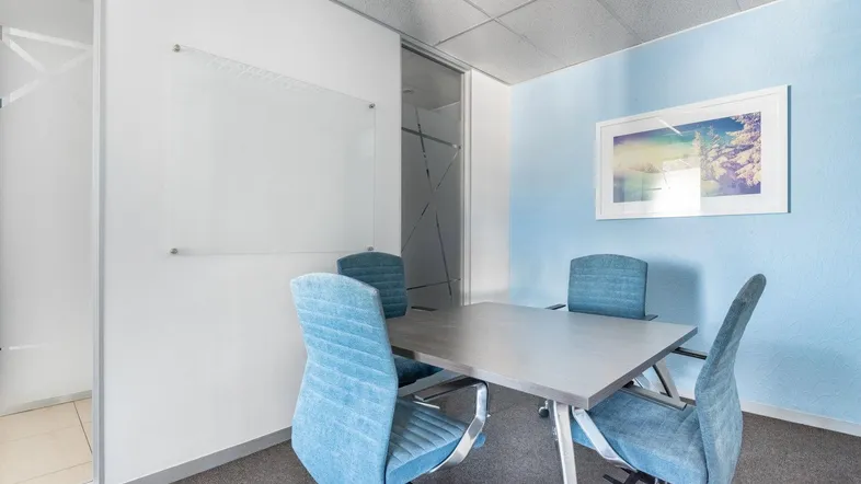 Modernes Besprechungszimmer mit blau gepolsterten Stühlen, einem grauen Tisch und einer Whiteboard-Wand für Notizen.