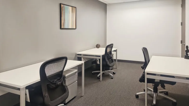 Modernes Büro mit mehreren Arbeitsplätzen, ergonomischen Stühlen und grauem Teppichboden für produktives Arbeiten.