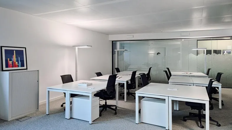 Moderner Büroraum mit mehreren Arbeitsplätzen, Teppichboden und Glaswänden zu weiteren Büros.