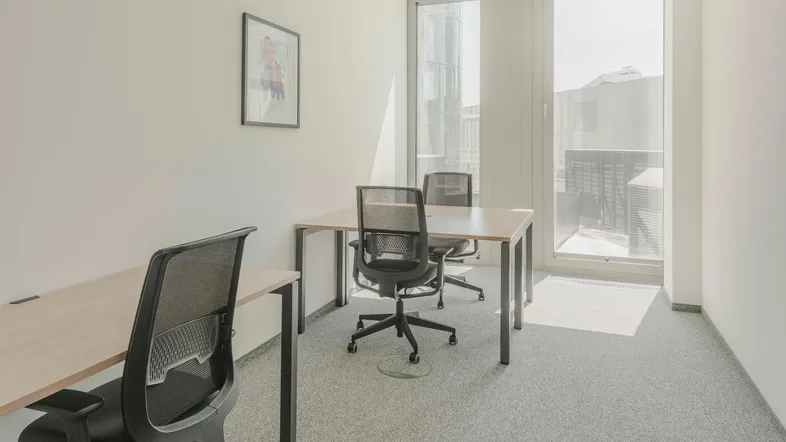 Helles Einzelbüro mit Teppichboden, zwei Schreibtischen und großen Fenstern für viel Tageslicht.
