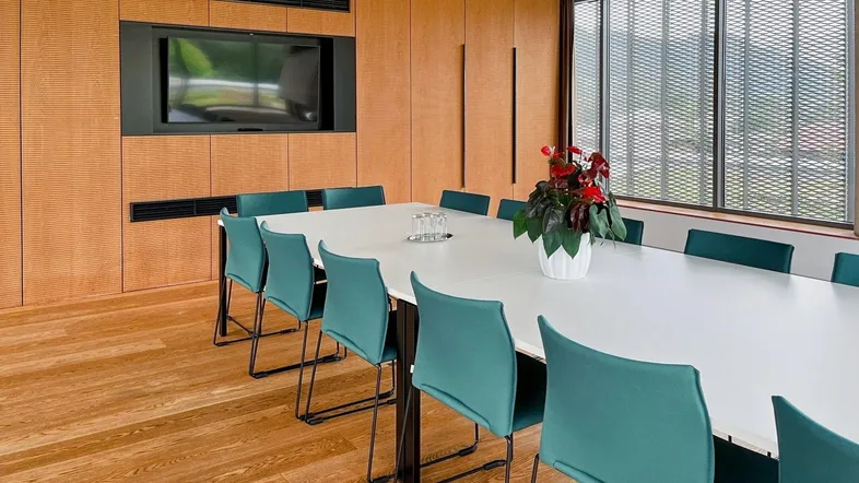 Moderner Konferenzraum mit Holzwänden, großem Tisch und integriertem Bildschirm für Präsentationen.