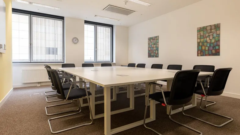 Großer Konferenzraum mit modernem weißen Tisch, bequemen Stühlen und Teppichboden, ideal für Besprechungen.