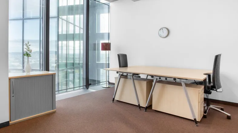 Modernes Büro mit großen Fenstern, Teppichboden und einem hellen Holzschreibtisch, ideal für konzentriertes Arbeiten.