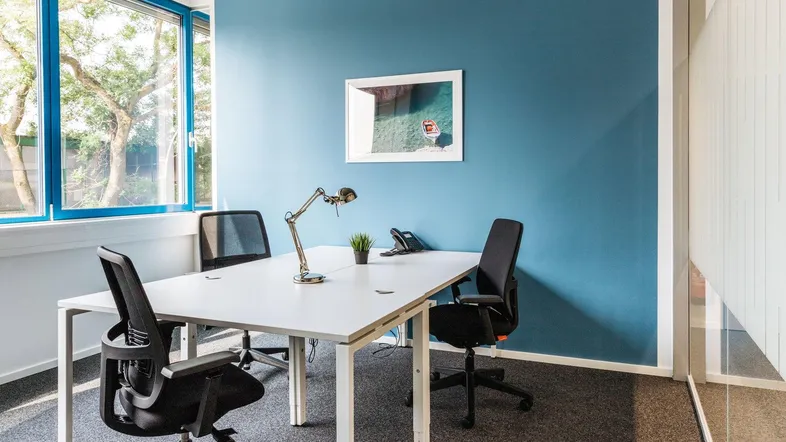 Modernes Büro mit blau gestrichener Wand, großem Fenster und zwei Arbeitsplätzen.
