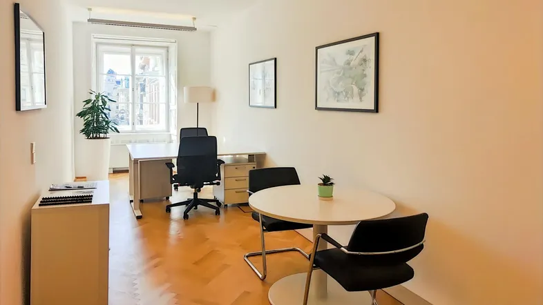 Helles Büro mit Fischgrätparkett, Schreibtisch und kleinem Besprechungstisch, ideal für produktives Arbeiten.