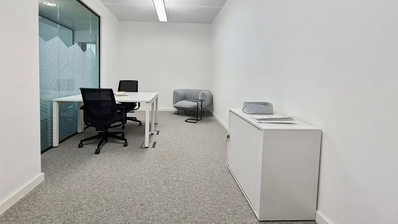 Modernes Büro mit Schreibtisch, Bürostuhl und einem kleinen Sessel, ideal für konzentriertes Arbeiten.