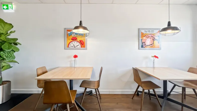 Heller Essbereich mit Holztischen, modernen Stühlen und dekorativen Bildern an der Wand für Pausen.