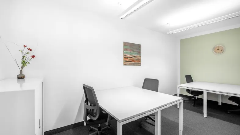 Helles Büro mit zwei Arbeitsplätzen, weißem Schrank und grüner Akzentwand, ideal für kleine Teams.