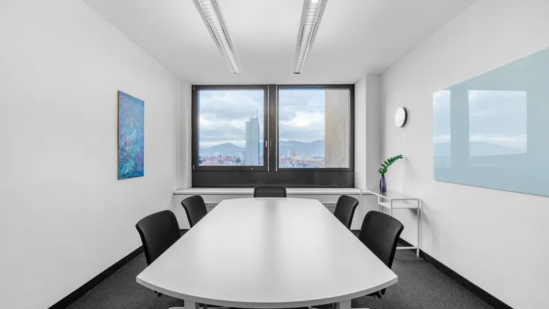 Moderner Konferenzraum mit großem Tisch, bequemen Stühlen und einem Fenster mit Stadtblick.