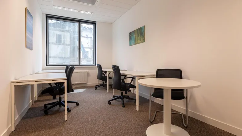 Modernes Büro mit mehreren Arbeitsplätzen, Teppichboden und großen Fenstern für natürliches Licht.