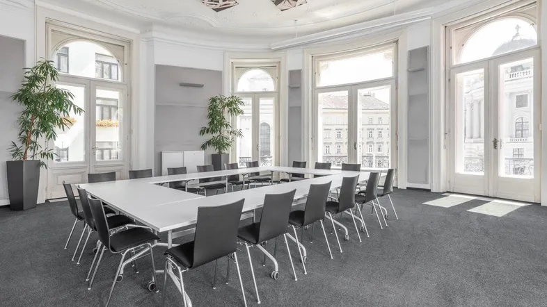 Großer Konferenzraum mit U-förmigem Tisch, vielen Stühlen und hohen Fenstern, ideal für Besprechungen.