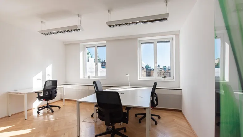 Helles Büro mit mehreren Arbeitsplätzen, großen Fenstern und Fischgrätparkettboden.