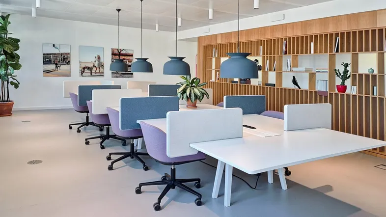 Moderner Großraumbüro-Arbeitsbereich mit Reihen von Schreibtischen, ergonomischen Stühlen und Holzregalen für Bücher.