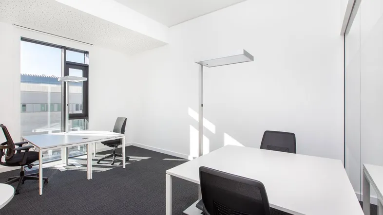 Helles und modernes Büro mit zwei Arbeitsplätzen, großen Fenstern und Teppichboden.