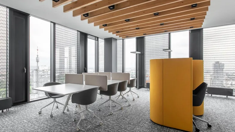Moderner Büroraum mit individuellen Arbeitsplätzen, großen Fenstern und Holzelementen an der Decke, bietet Stadtblick.