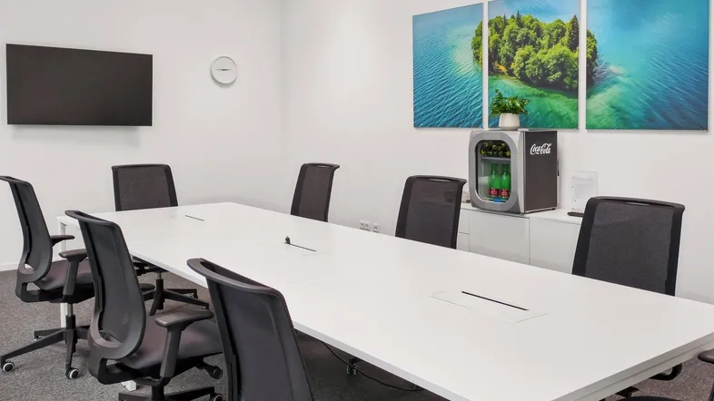 Moderner Konferenzraum mit großem weißen Tisch, ergonomischen Stühlen und Wandbildern mit Seeblick.