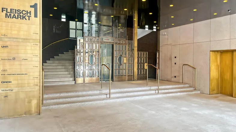 Elegante Lobby mit goldfarbenen Aufzügen, einer breiten Treppe und einem modernen Firmenverzeichnis.