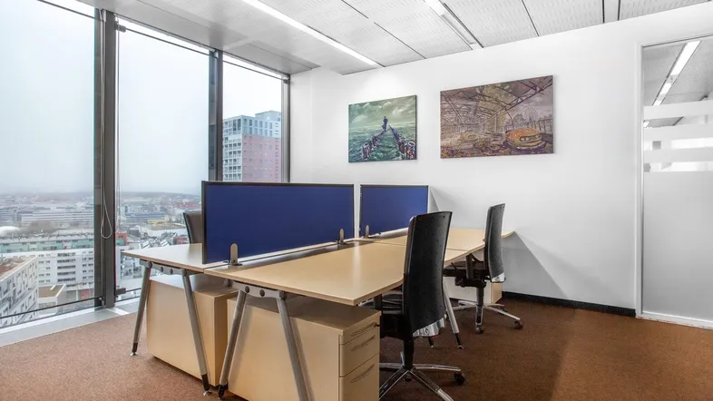 Modernes Büro mit mehreren Arbeitsplätzen, großen Fenstern und Blick auf die Stadt.