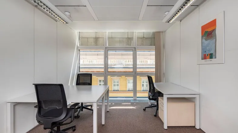 Modernes Büro mit zwei Arbeitsplätzen, großen Fenstern und Teppichboden, ideal für konzentriertes Arbeiten.