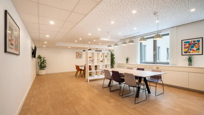 Großer, offener Bürobereich mit Holzboden, langen Tischen und modernen Möbeln für Zusammenarbeit.