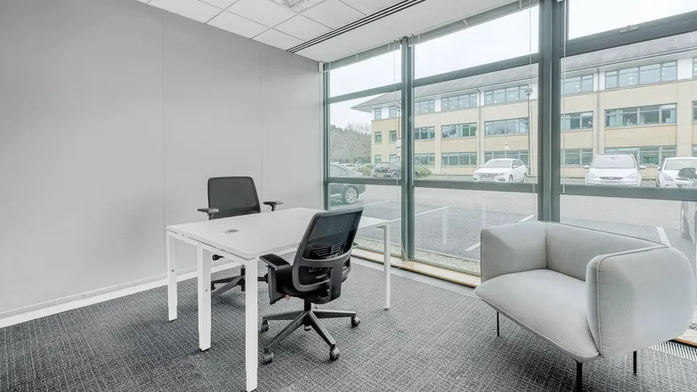 Helles Büro mit großen Fenstern, Blick auf den Parkplatz und moderne Büromöbel für Besprechungen.