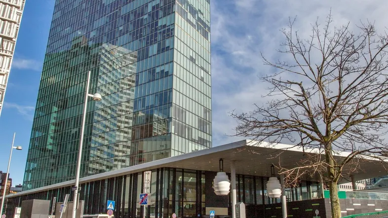 Modernes Hochhaus mit Glasfassade und umliegender Infrastruktur an einem sonnigen Tag.