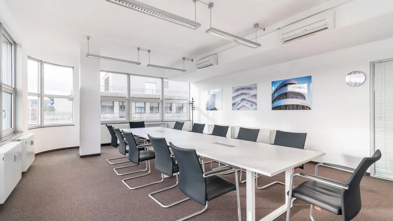 Heller Konferenzraum mit großem Tisch, ergonomischen Stühlen und Blick auf die Stadt.