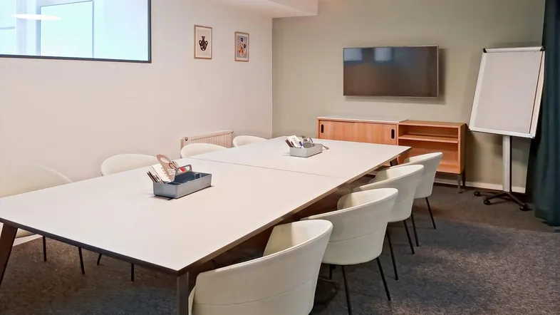 Modern eingerichteter Konferenzraum mit großem Tisch, bequemen Stühlen und einem Flatscreen-TV.